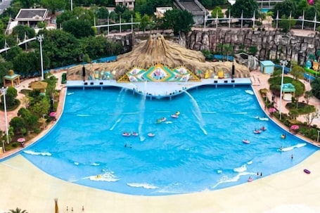A large swimming pool with multiple lanes, surrounded by a tropical-themed area with a thatched-roof structure.. Jinfan City Hotel