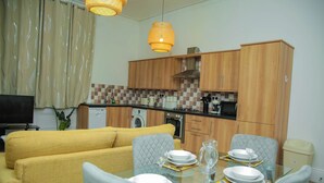 Eine moderne Küche mit Holzausbau, einem Esstisch gedeckt mit Geschirr und Gläsern, sowie ein gelbes Sofa im Wohnbereich.