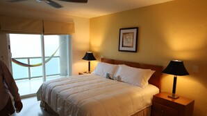 A hotel room with a large bed, two bedside tables with lamps, a framed artwork on the wall, and a view through a window with a hammock. - 4/4.5 Condo Oceanfront Cozumel Downtown AC WiFi Security (Cozumel)