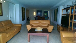 A living room with a brown leather sofa, a wooden coffee table, and a bookshelf. - 4/4.5 Condo Oceanfront Cozumel Downtown AC WiFi Security (Cozumel)
