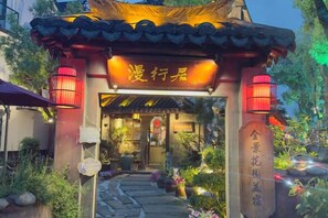 Una puerta china tradicional con faroles iluminados, un letrero y un camino que lleva a un edificio.