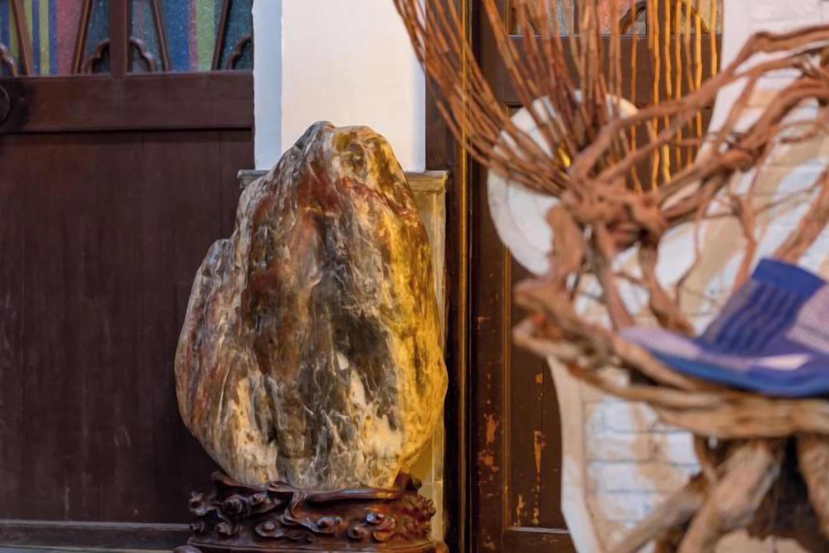 A large rock sculpture on a pedestal, a wicker chair, and a wooden door.