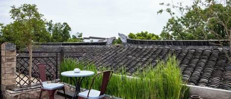 An outdoor seating area with a table and chairs, a stone wall, and a traditional tiled structure in the background.