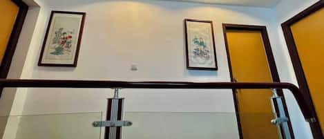 A hallway with a handrail, two doors, and two framed artworks on the wall.