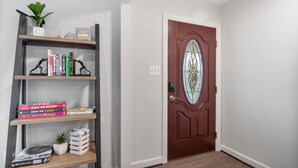 A hallway with a wooden bookshelf containing books and a small plant. A red door with a glass panel is visible. - Spacious 8 beds LUX convenient Home close to DC (Bethesda)