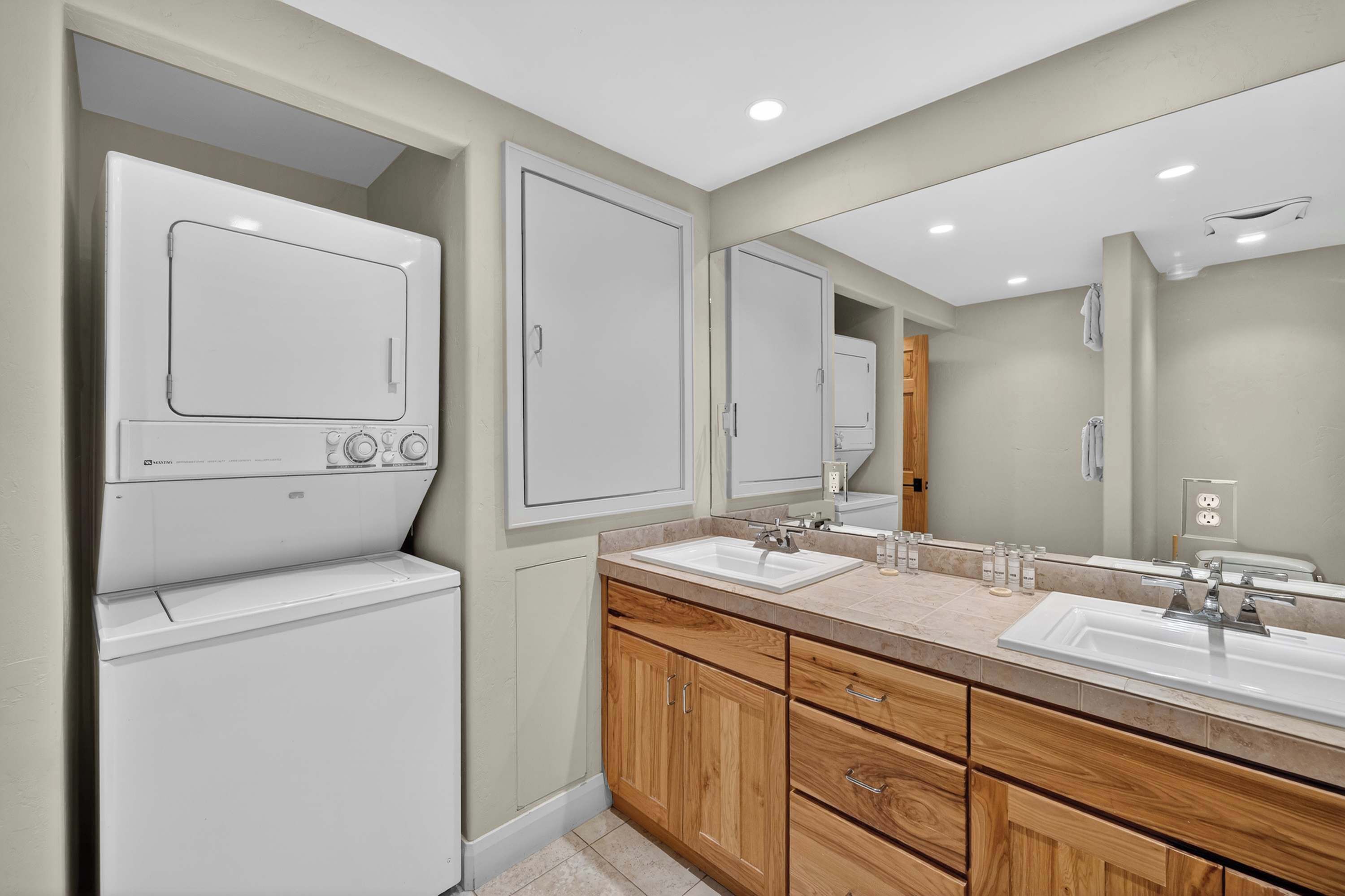 A modern bathroom with a double sink, wooden cabinets, a large mirror, and a built-in washer and dryer.