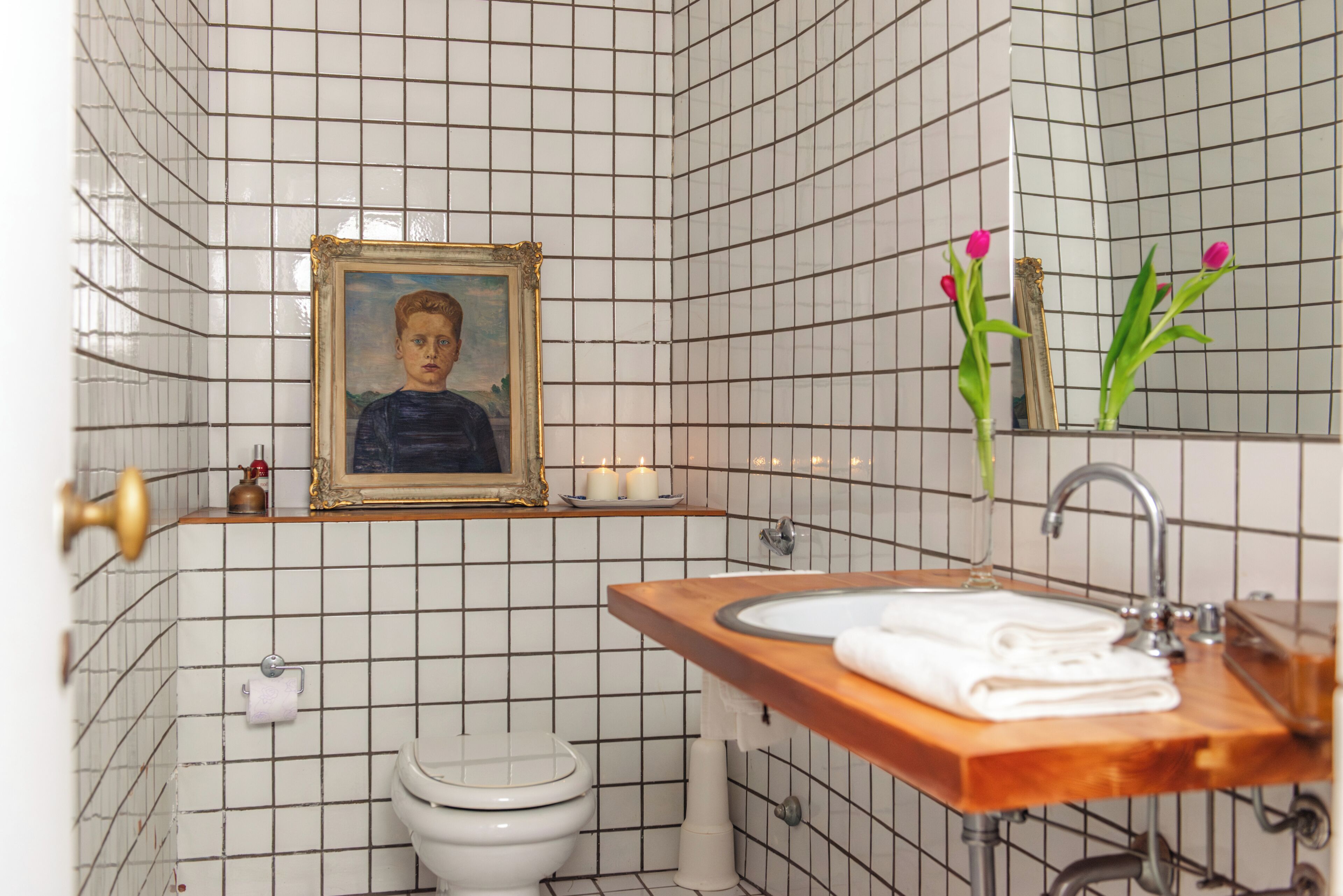 Ein Badezimmer mit gefliesten Wänden, einem gerahmten Gemälde, einem Waschbecken mit Holzablage und einer Toilette.