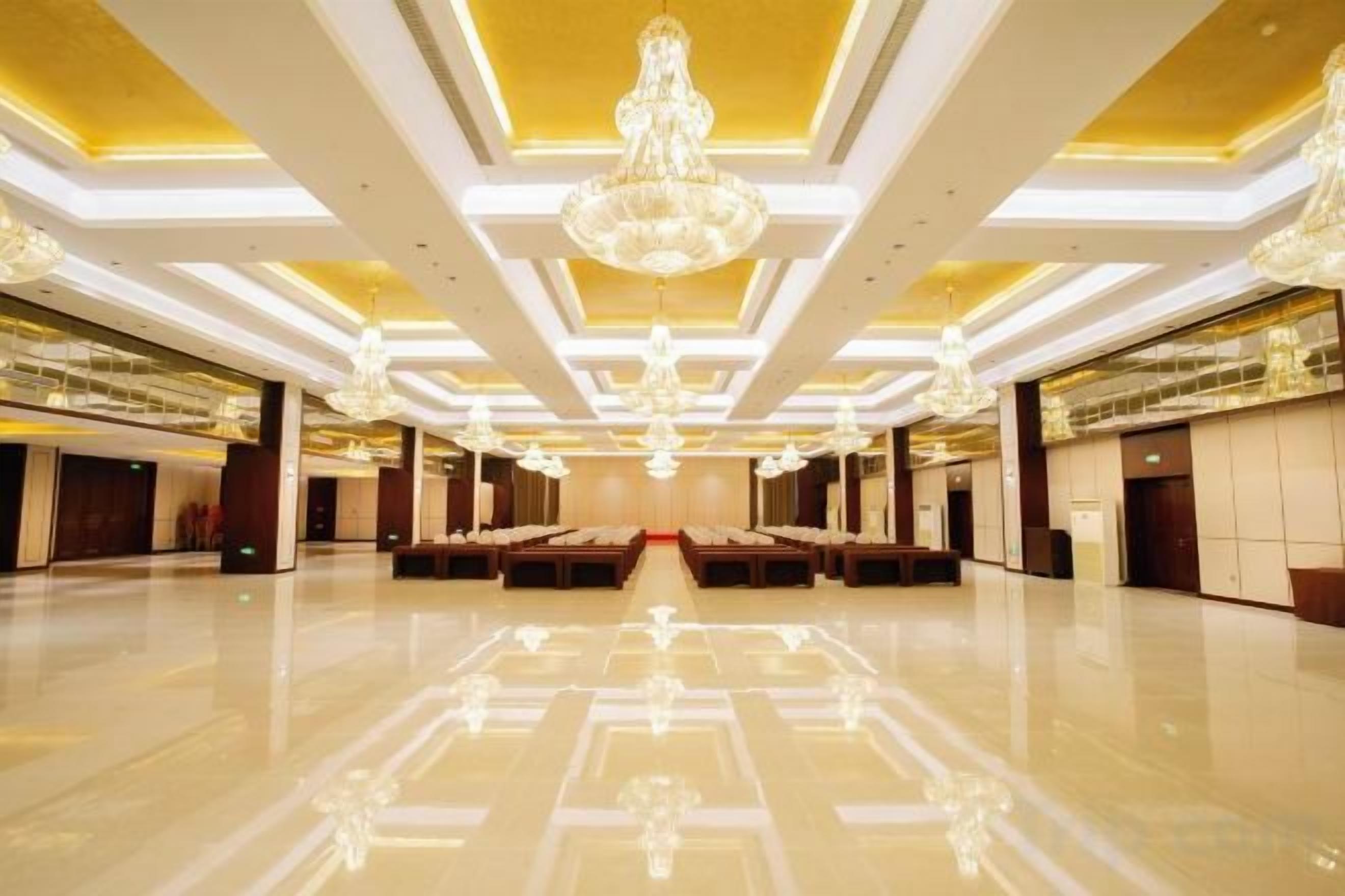 A spacious hotel lobby with a reflective floor, multiple seating areas, and large chandeliers.