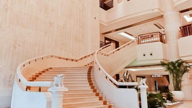 A multi-level interior with a central staircase, white railings, and decorative statues. - Fucheng International Hotel (Sanhe)