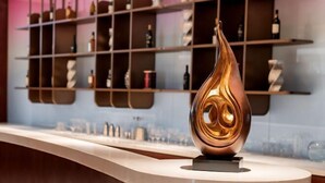 Un espace bar moderne, agrémenté d’une sculpture métallique originale qui en constitue l’élément central, d’étagères remplies de bouteilles et d’un comptoir élégant.