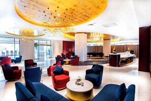 Eine großzügige Lobby mit mehreren Sitzbereichen, einem runden Tisch in der Mitte und einem markanten Deckenstil.