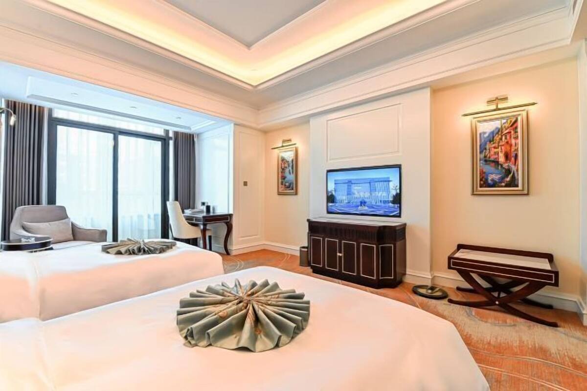 Une chambre d’hôtel avec deux lits, une télévision, un bureau et une grande fenêtre.