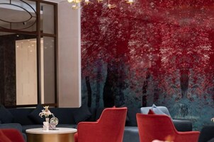 Un interior moderno con un mural abstracto rojo y azul, una mesa redonda dorada con un florero y un globo terráqueo, y sillas tapizadas en rojo y negro.
