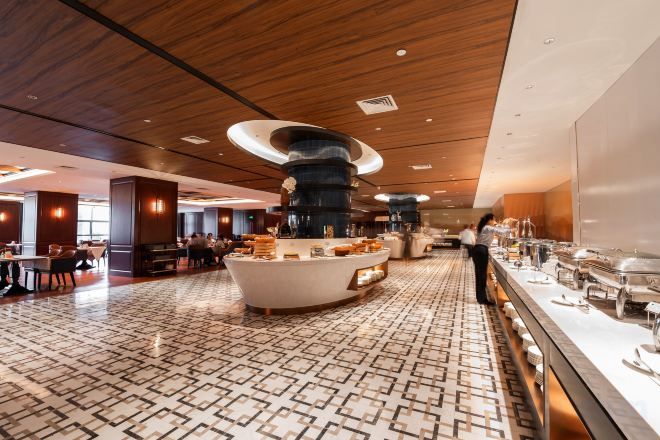 A spacious hotel lobby with a central island, seating areas, and a buffet setup.