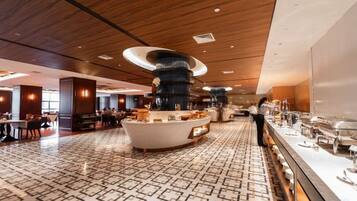 A spacious hotel lobby with a central island, seating areas, and a buffet setup.