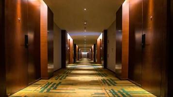 A hotel corridor with doors on both sides, a patterned carpet, and a ceiling with recessed lighting.