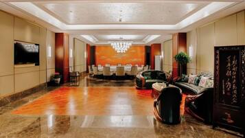 A hotel lobby with a reception desk, seating area, and a chandelier.