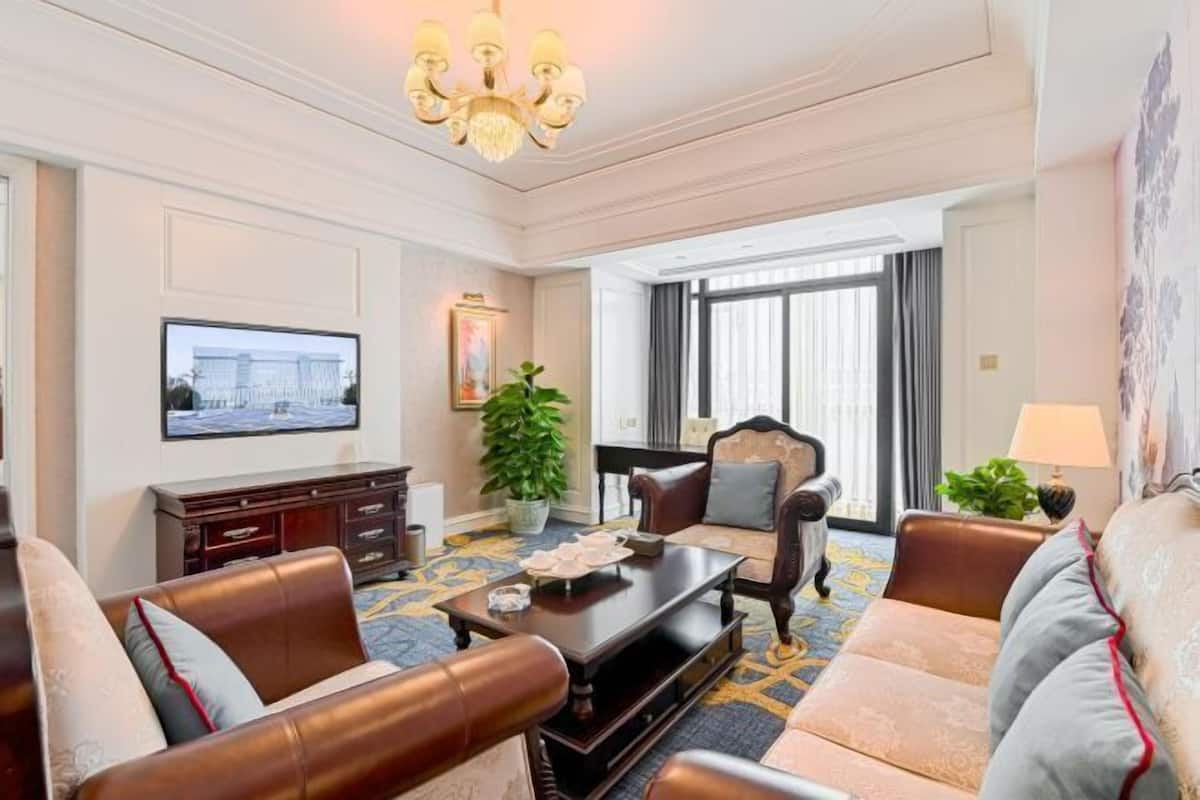 Une chambre d’hôtel dotée d’un espace salon comprenant des canapés en cuir, une table basse, un téléviseur, une plante en pot et un lustre.