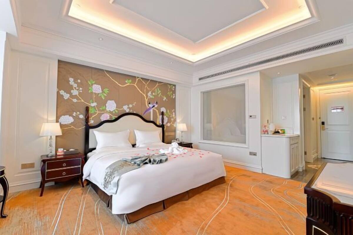 Une chambre d’hôtel avec un grand lit, une table de chevet, une commode et une grande fenêtre.