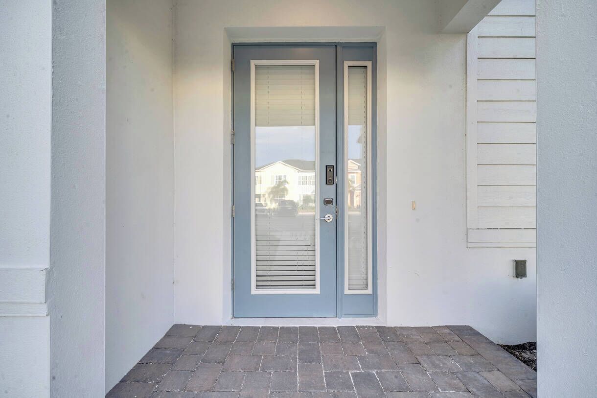 Puerta principal con panel de vidrio corredera, timbre y buzón pequeño.