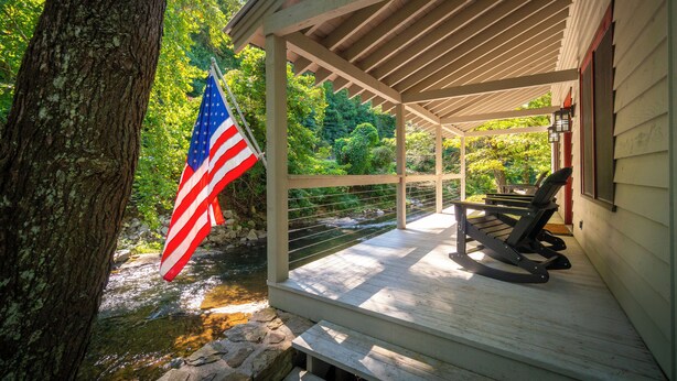 Overdekt terras met uitzicht op een beek, een Amerikaanse vlag en twee schommelstoelen.