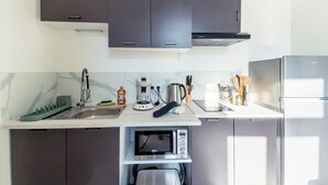 A modern kitchen with dark cabinets, a built-in microwave, a coffee maker, and a stainless steel refrigerator. - Cosy T2 completely renovated (Villeurbanne)