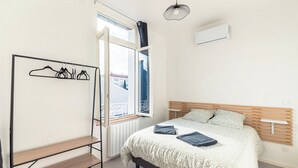 A bedroom with a bed, a window with a view, a radiator, and a wall-mounted air conditioner. - Cosy T2 completely renovated (Villeurbanne)
