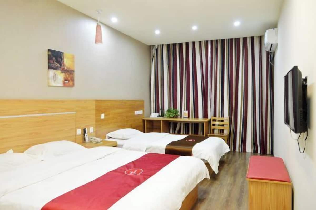 A hotel room with two beds, a desk, a chair, a television, and a striped curtain.