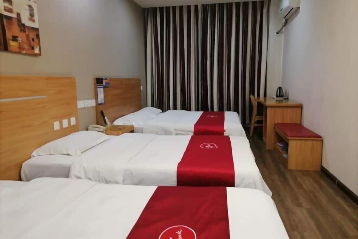 A hotel room with three beds, a wooden headboard, a desk, a chair, a small table, and a curtain.