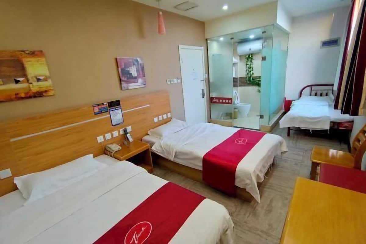 A hotel room with two beds, a wooden headboard, a small table, and a glass-enclosed shower area.