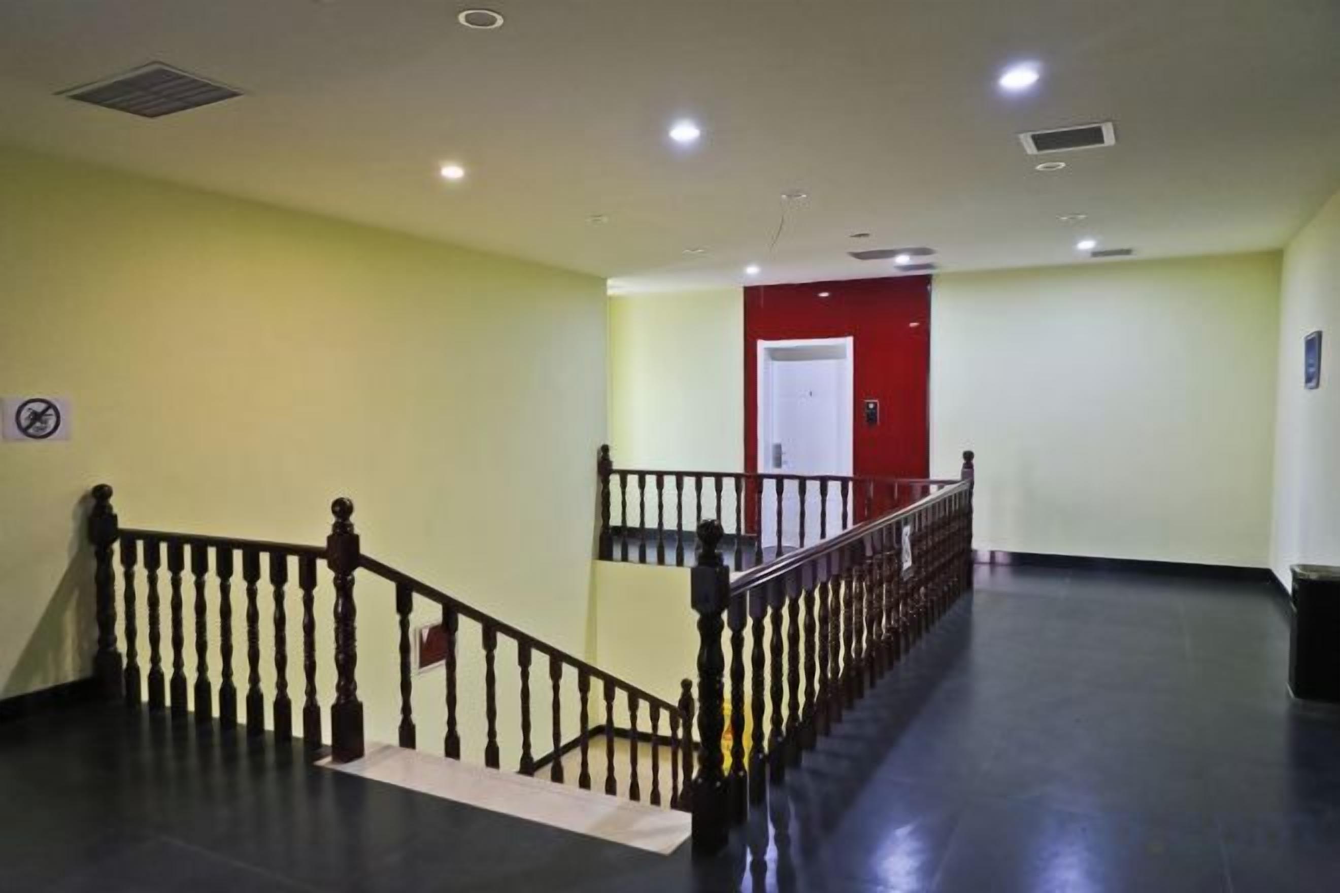 A hotel corridor with a black railing, a red door, and a white wall.