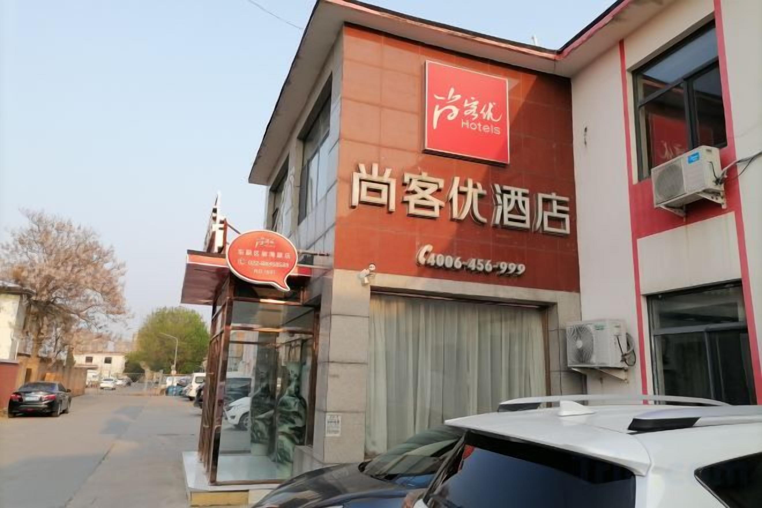 A hotel with a red and white facade, a visible entrance, and a contact number.