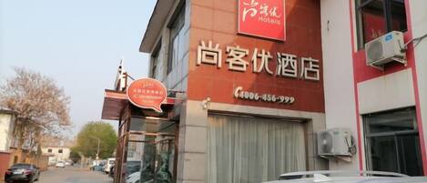 A hotel with a red and white facade, a visible entrance, and a contact number.