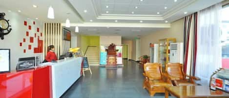 A hotel reception area with a red counter, a clock, and a staircase in the background.