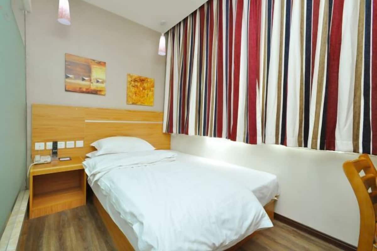 A hotel room with a single bed, a wooden nightstand, a chair, and a striped curtain.