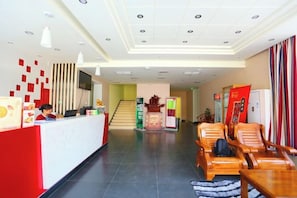 A hotel reception area with a reception desk, seating area, and a staircase leading to other floors.