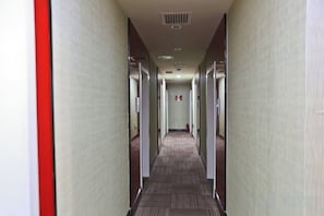 A hotel corridor with doors on both sides, a carpeted floor, and a fire alarm on the wall.