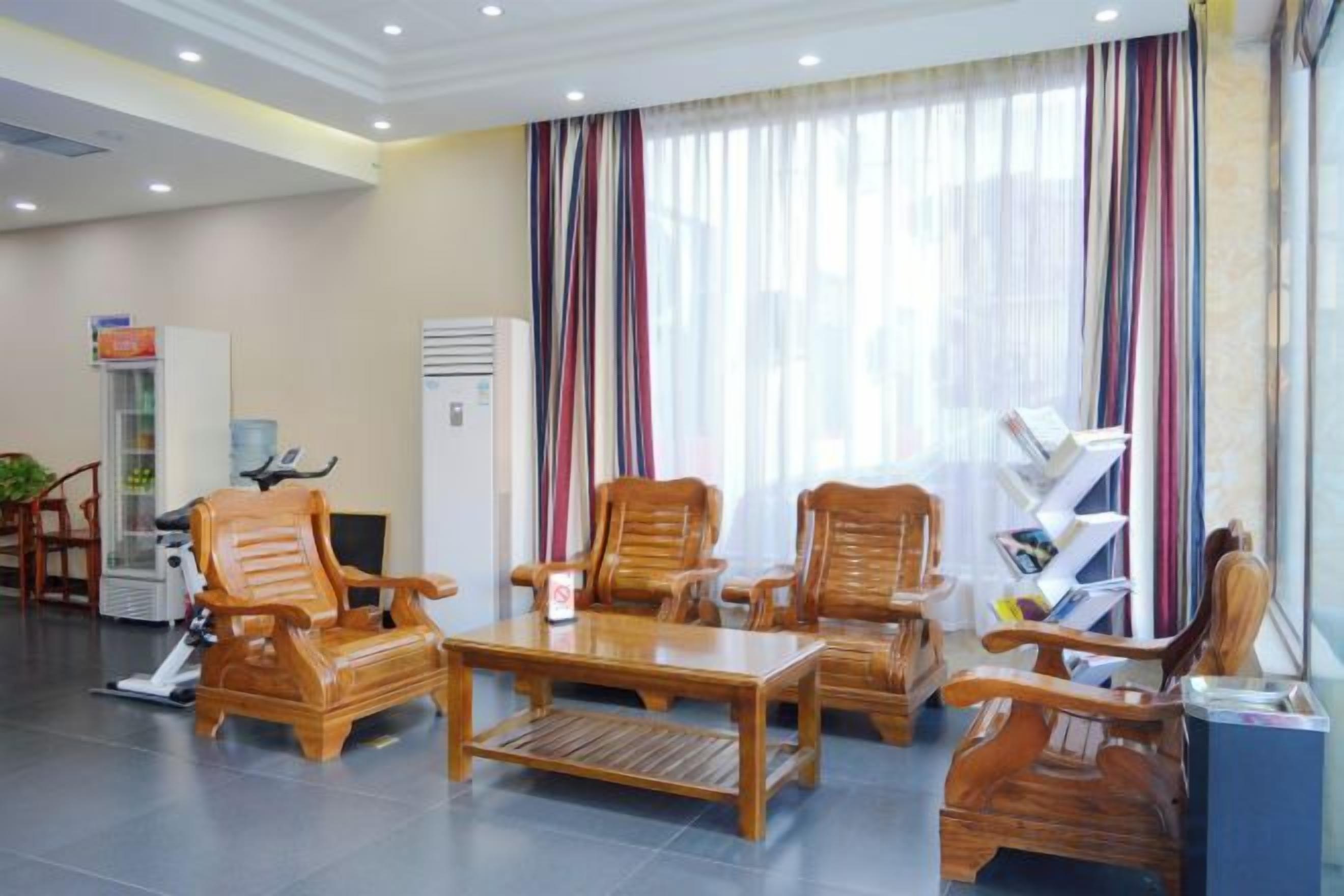 A hotel lobby with wooden furniture, a reception desk, and a large window with curtains.