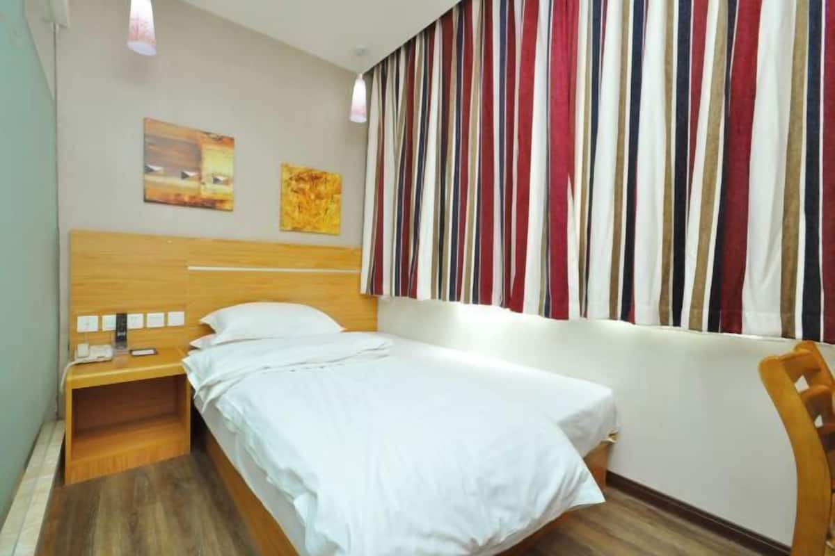 A hotel room with a wooden bed, a nightstand with a phone and a lamp, striped curtains, and two paintings on the wall.
