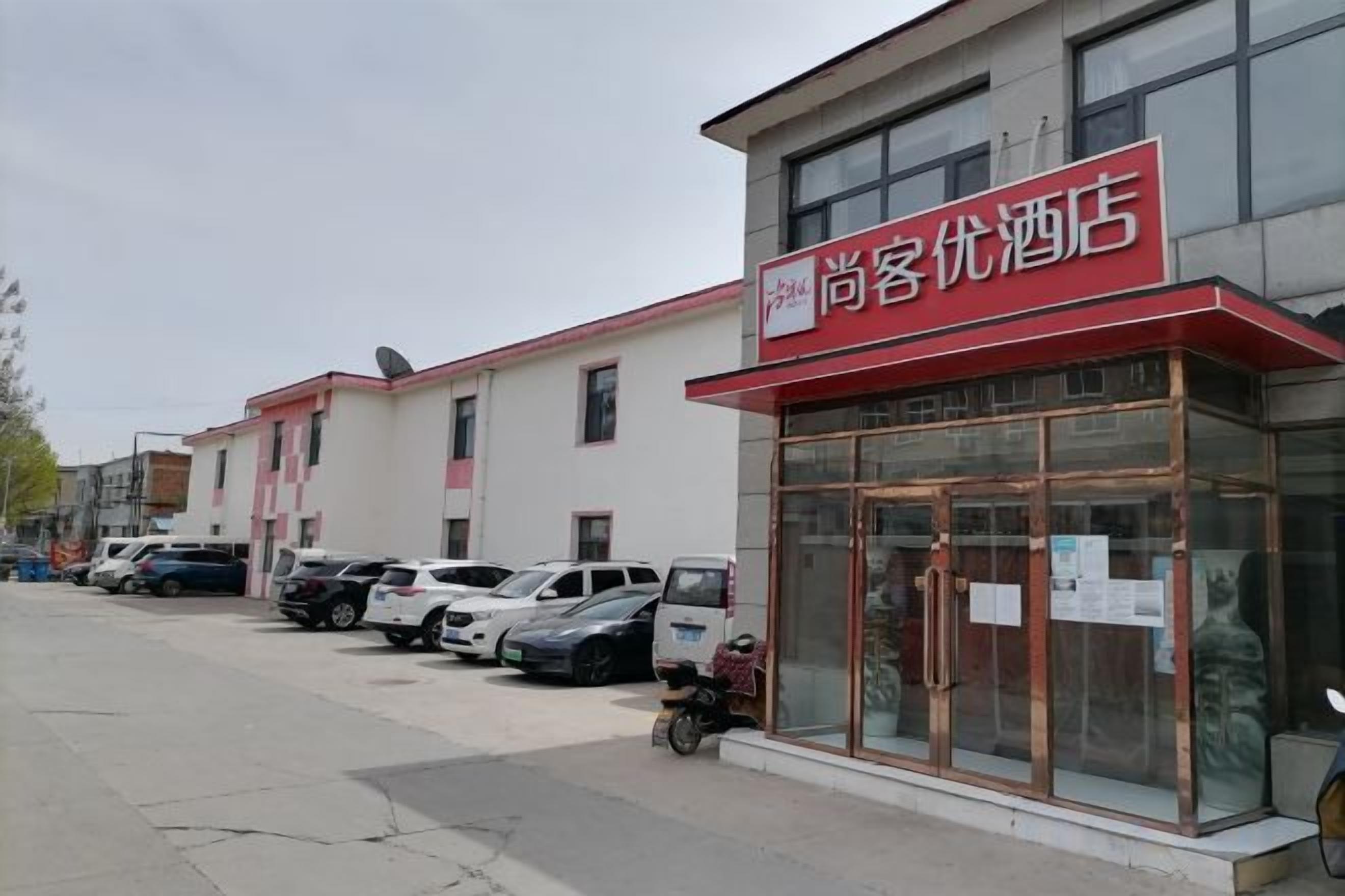 A hotel with a red awning and a glass facade. There are several cars parked in front.