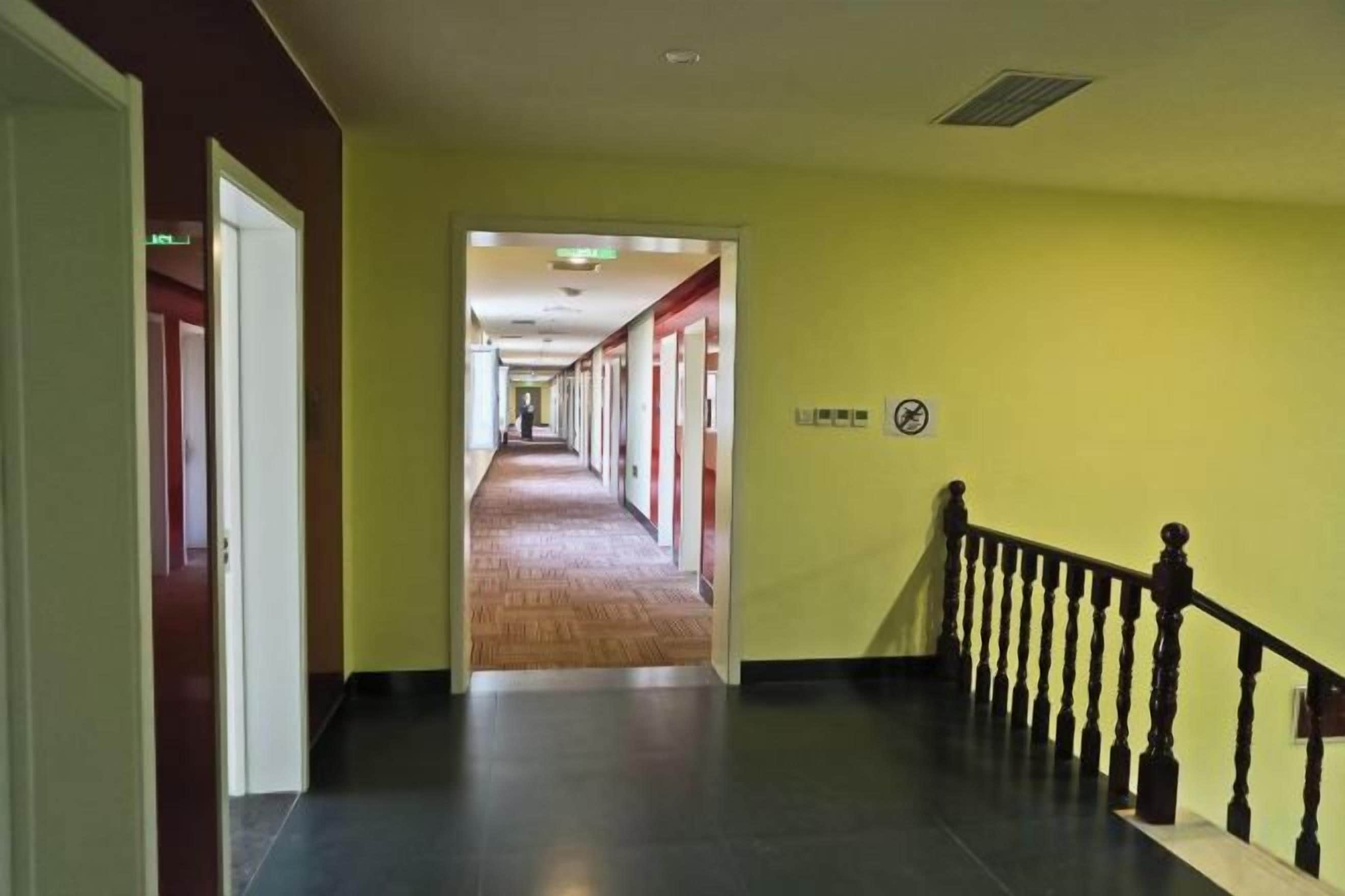 Un couloir doté d’un plancher en bois, d’un escalier avec une rampe noire et d’un mur jaune.