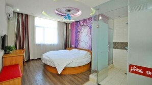 Une chambre avec un lit rond, un bureau, une chaise, un banc rouge, une cabine de douche en verre et une fresque murale.