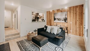 Een moderne woonkamer met een donkergrijze bank, een zwart voetenbankje en een houten wandpaneel.