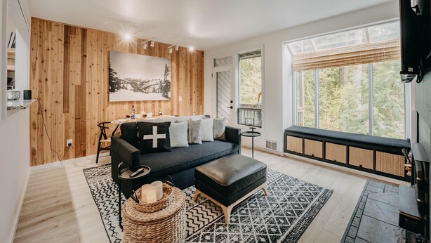 Een moderne woonkamer met een donkere bank, een salontafel en een groot raam met uitzicht op bomen.
