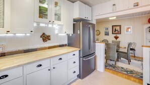 A kitchen with white cabinets, a stainless steel refrigerator, and a wooden countertop. There is a dining area with chairs and a table. - Unwind Fireside & Walk to Dtwn! Tyron Retreat (Tryon)
