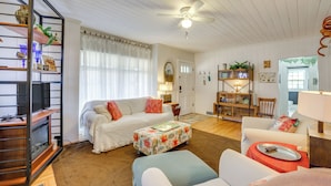 A cozy living room with a white sofa, a floral ottoman, and a wooden bookshelf. - Unwind Fireside & Walk to Dtwn! Tyron Retreat (Tryon)