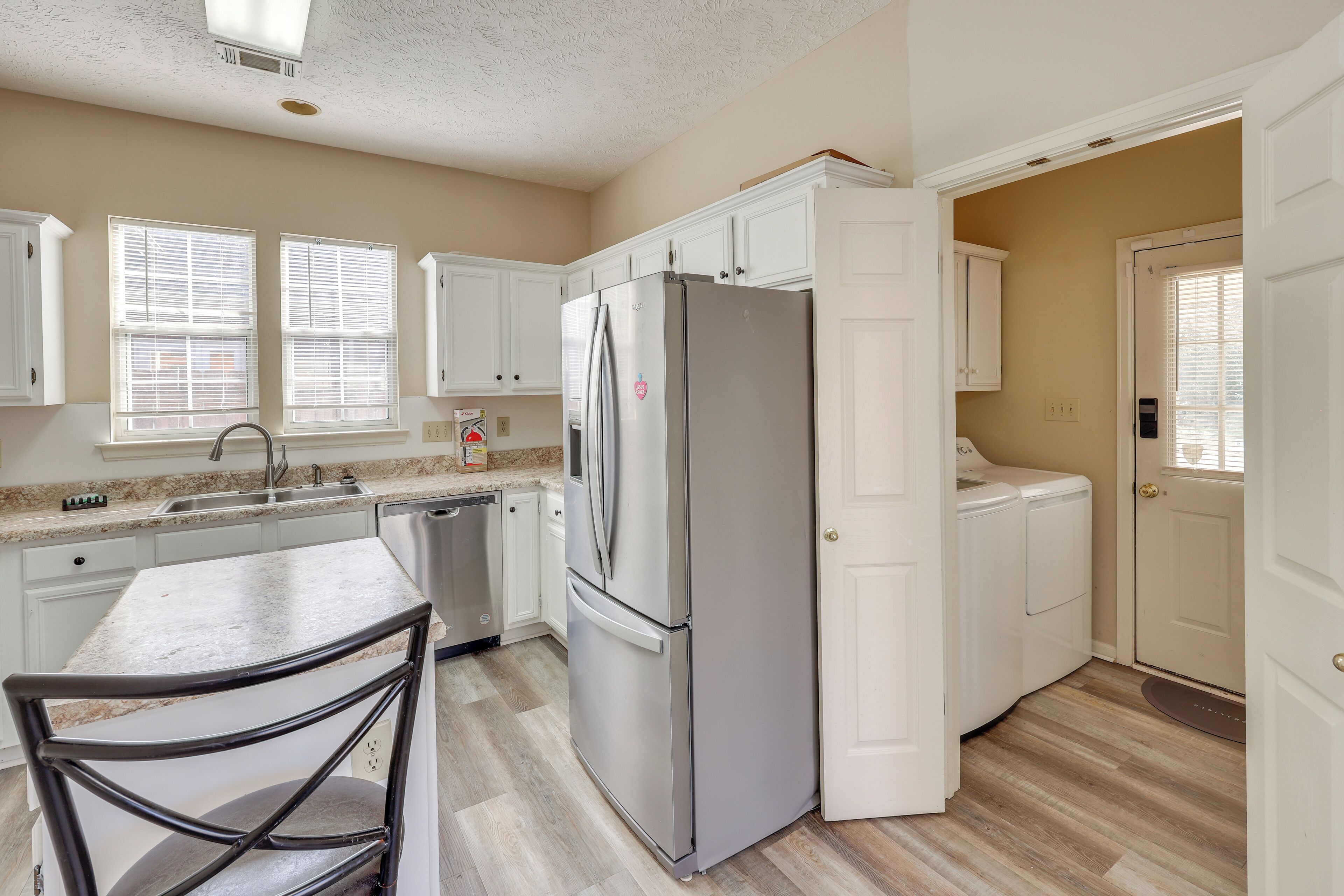 A kitchen with white cabinets, a stainless steel refrigerator, a granite countertop, and a bar stool.