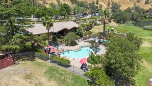 An aerial view of a resort with a swimming pool, palm trees, and a golf course in the background.