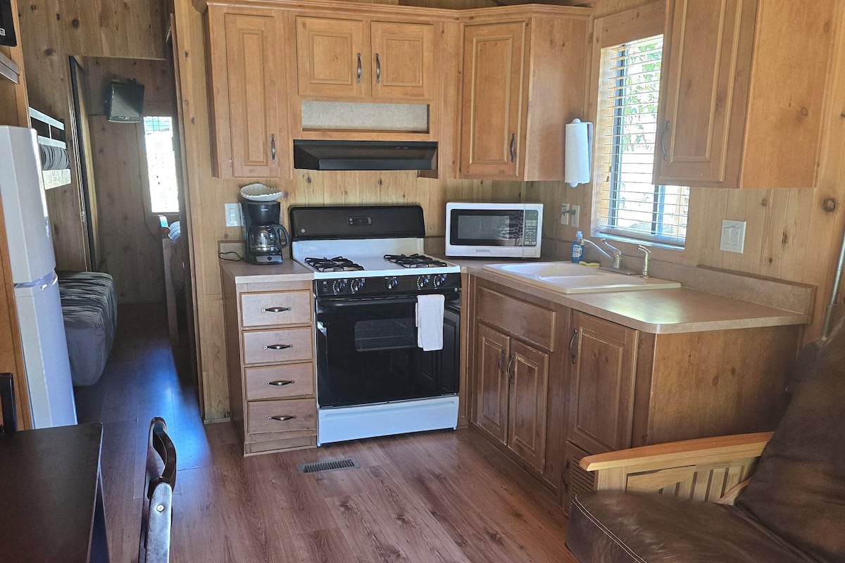 A compact kitchen with wooden cabinets, a stove, a microwave, and a sink.