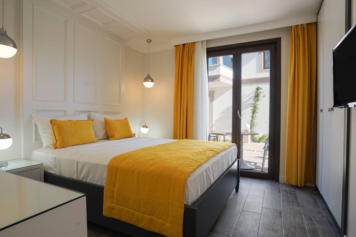 A hotel room with a bed, bedside lamps, a flat-screen TV, and a view of the outside.
